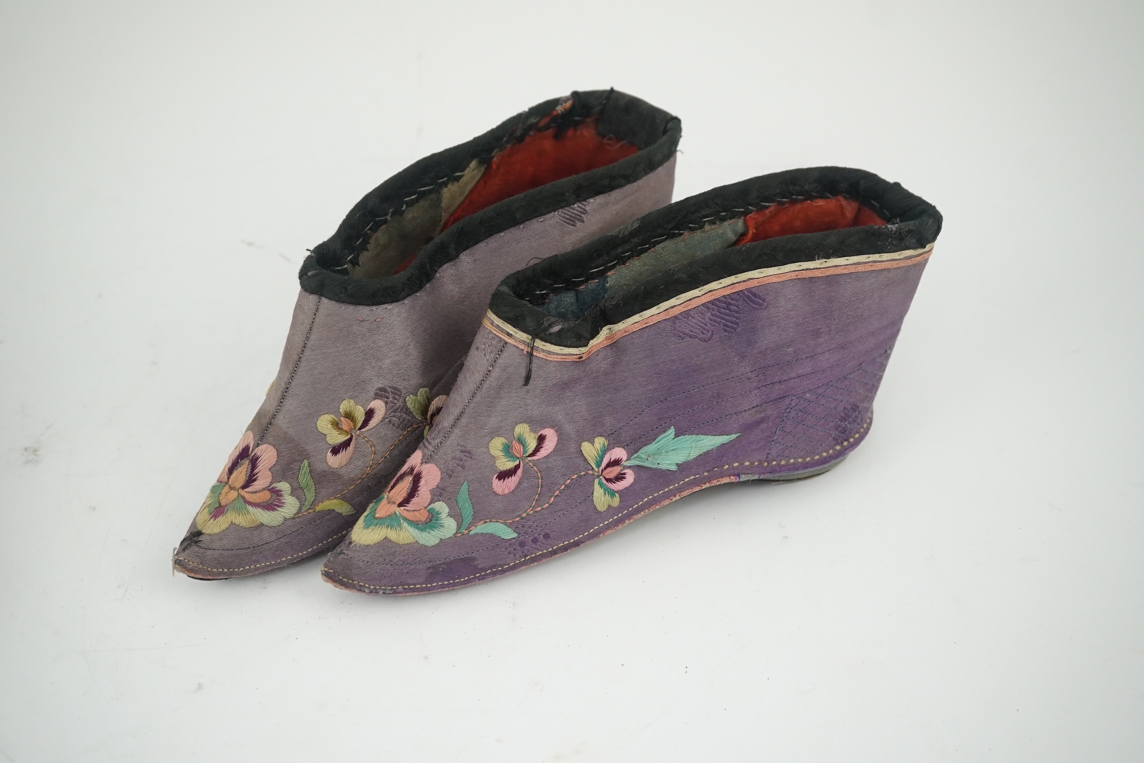 Four pairs of late 19th / early 20th Chinese ladies bound foot shoes, made in various coloured silks, with colourful floral embroidered motifs, two pairs with decorative silk pom-poms and another made of purple and black